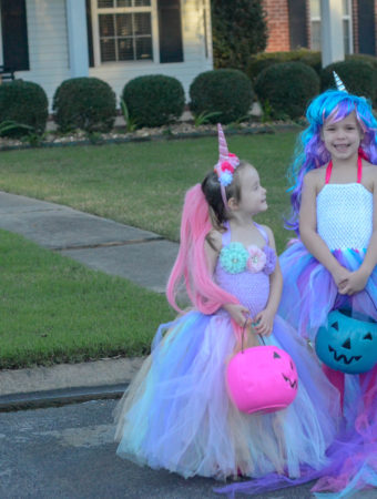 two girls in unicorn Halloween costumes with candy buckets
