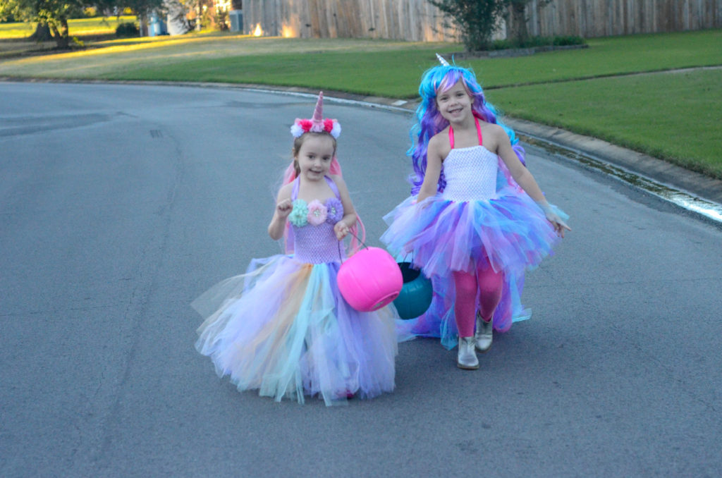 two girls in unicorn Halloween costumes with candy buckets 