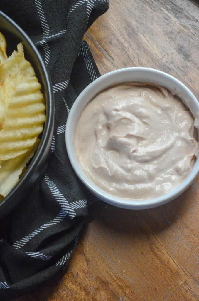 white barbecue sauce in white bowl with black napkin and bowl of potato chips