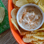 bbq sour cream dip in white bowl with potato chips in orange platter