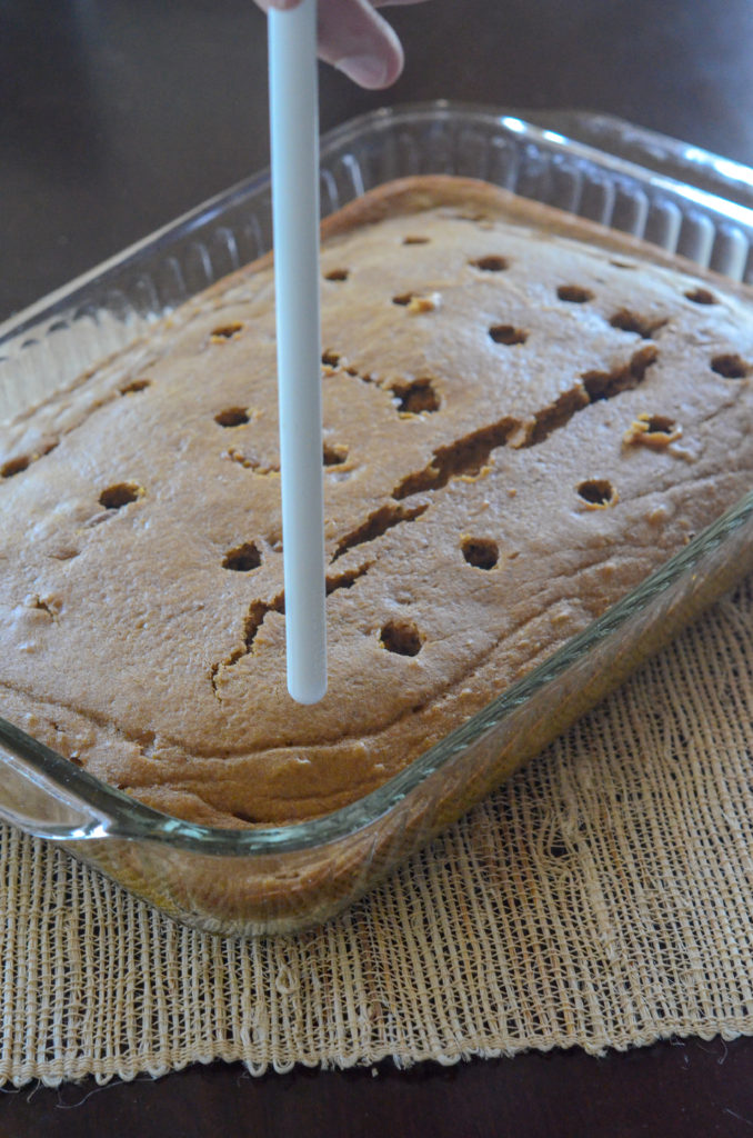 a wooden spoon punches holes into pumpkin spice poke cake
