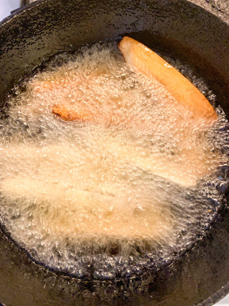 yuca sticks frying in hot oil in cast iron skillet