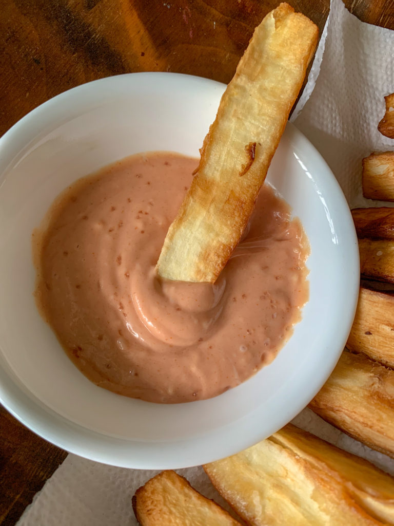 yuca fries dipped into spicy yuca sauce in white bowl 
