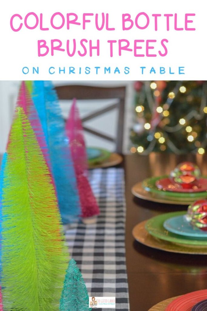 a Christmas table set with bottle brush trees, place settings and a Christmas tree in the back