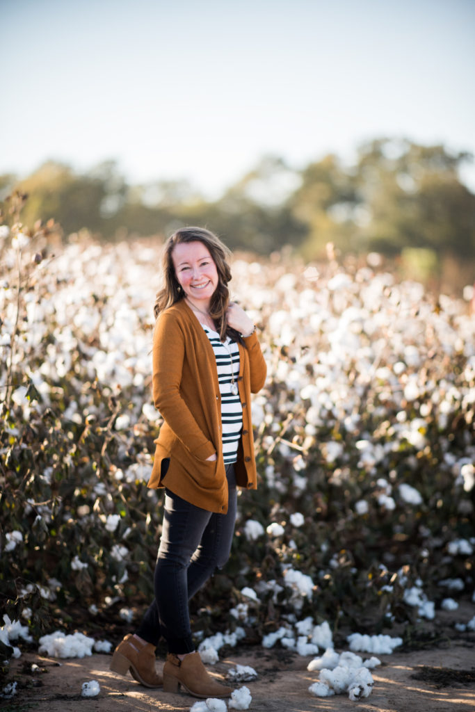 lady stands in front of cotton field in brown cardigan with striped shirt