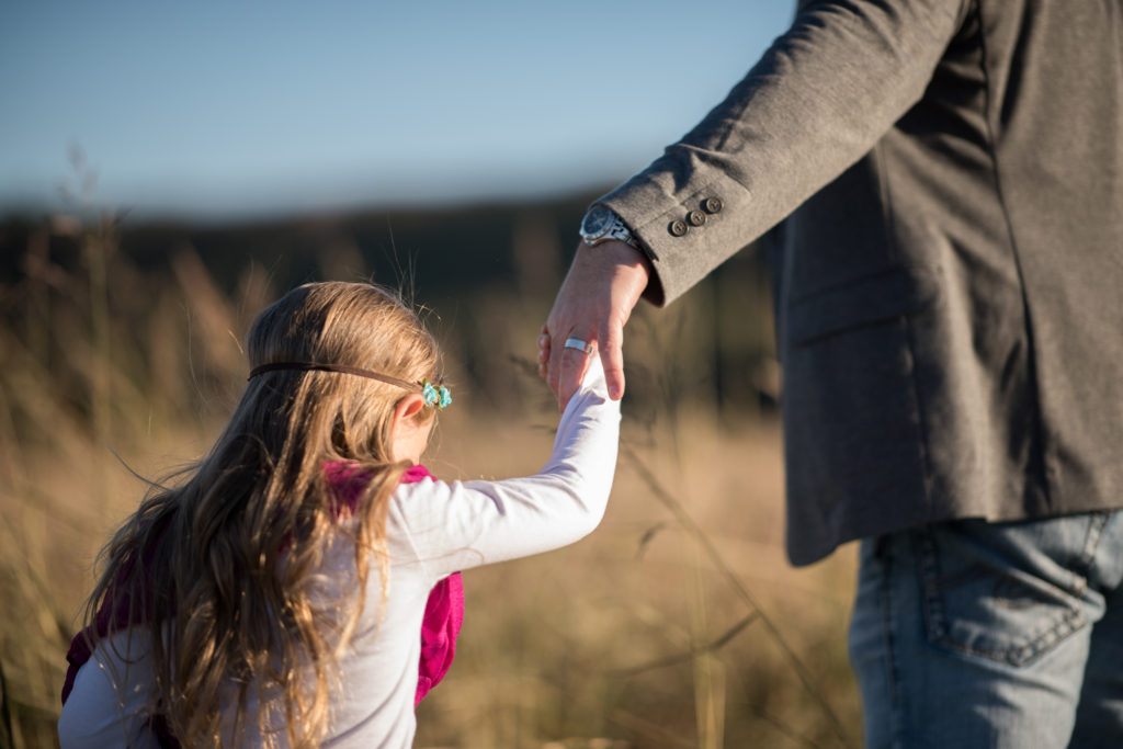 little girl holds daddy's hand in field