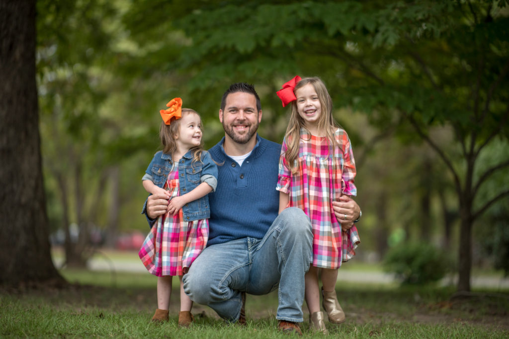 dad poses with little girls wearing matching blue and mustard outfits with plaid for casual fall outfits