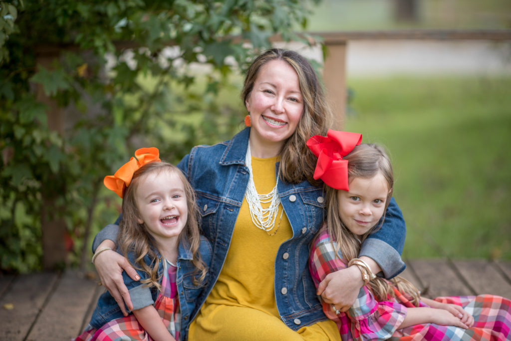 a mom in blue and mustard yellow poses with two daughters wearing casual fall outfits for fall family photoshoot