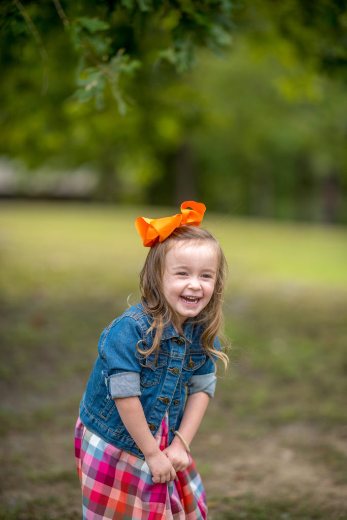 little girl in plaid dress and blue jean jacket laughing during a fall family photoshoot