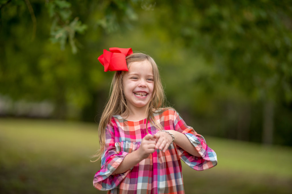 little girl with red bow and plaid dress during a fall family photoshoot 