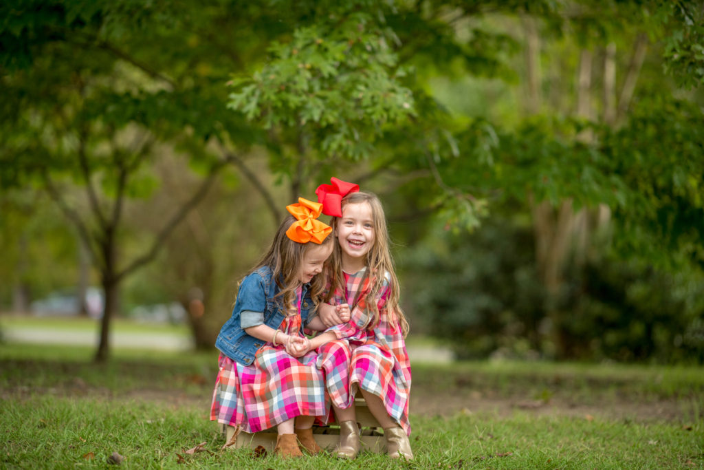 two matching sisters in plaid dresses sitting on wooden pallet during a fall family photoshoot