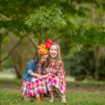 two matching sisters in plaid dresses sitting on wooden pallet