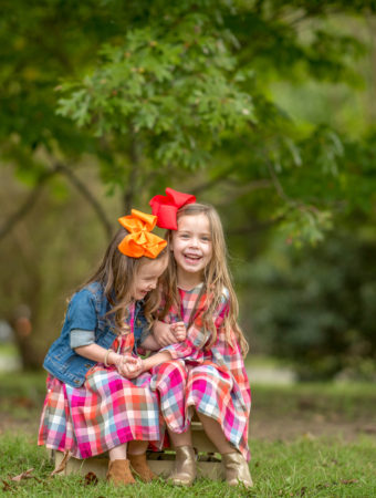 two matching sisters in plaid dresses sitting on wooden pallet