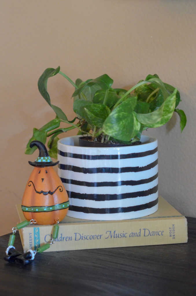 smiling pumpkin on top of old books with pothos in striped planter