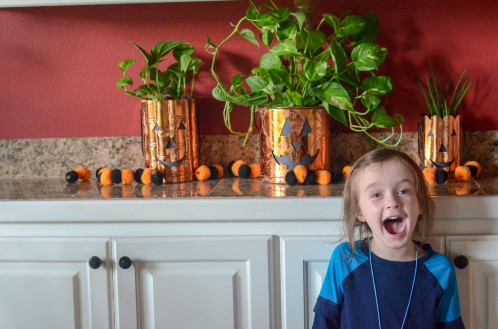 little girl makes scary face in front of Halloween plants in jack o lantern plant pots