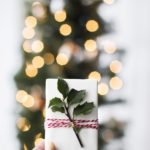 woman holds wrapped Secret Santa present in front of Christmas tree