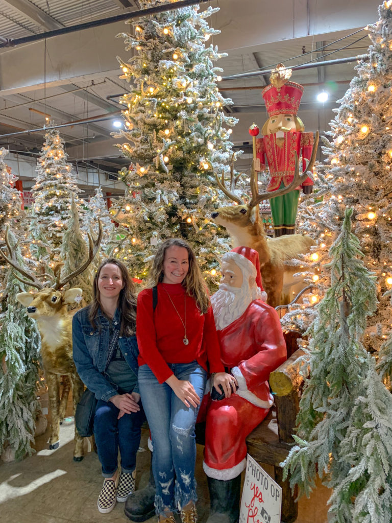 ladies pose with ceramic Santa amid lit Christmas trees and Guess and Company Christmas Warehouse in Des Arc