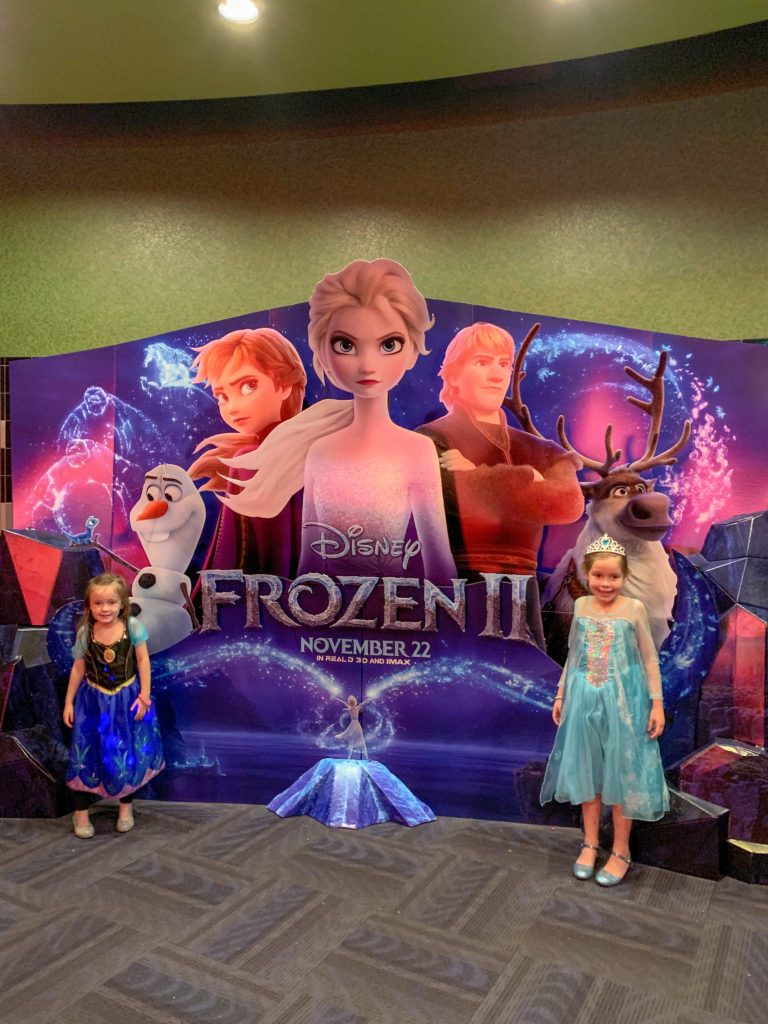 two girls pose under Frozen 2 promotional poster during a movie theater birthday party at the Rave theater in Little Rock, AR