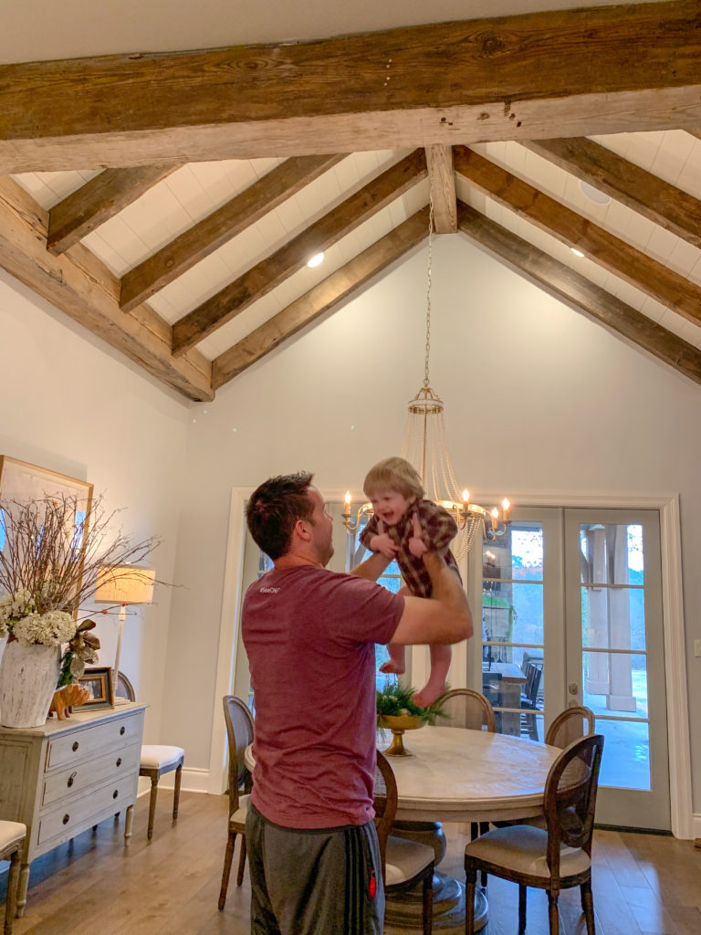 man plays with baby in modern farmhouse dining room with wood beams