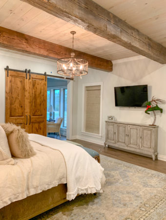 bed with neutral linens and real wood beams on ceiling and barn door