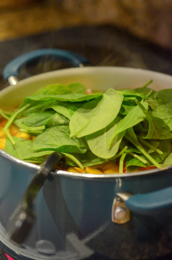 baby spinach piled on top of pot of tortellini for a spinach tortellini black eyed pea soup