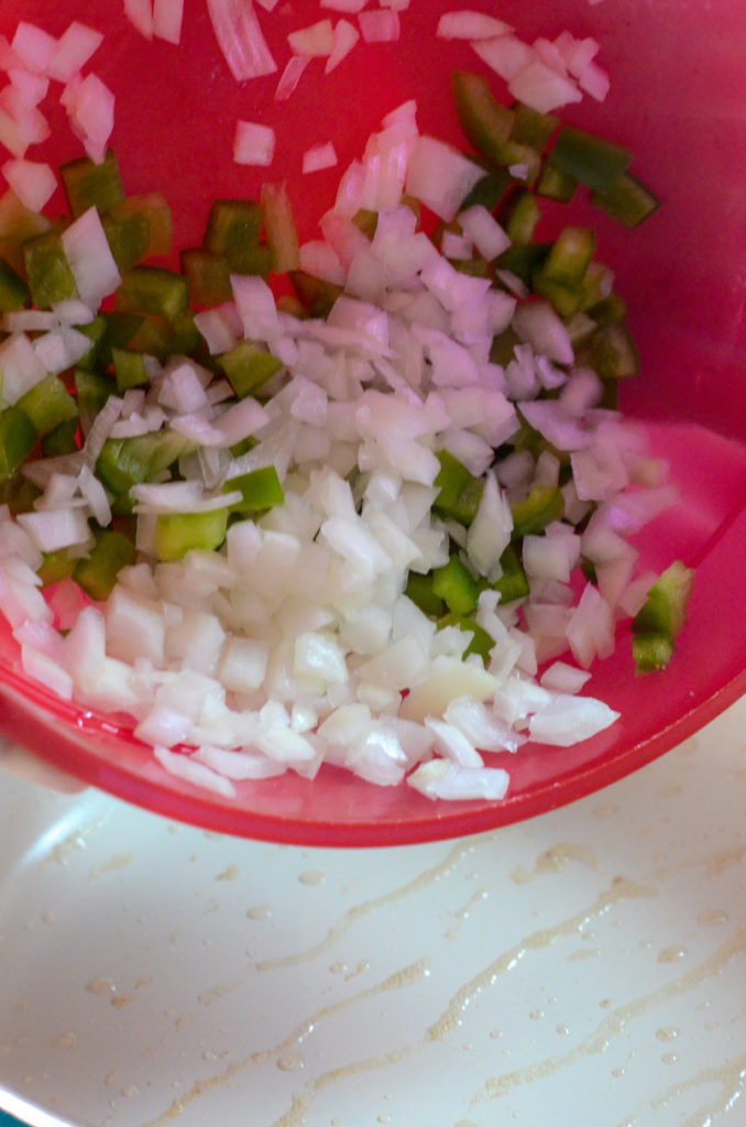 mixture of onions and bell peppers being poured into skillet