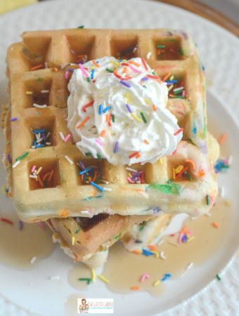 funfetti waffles on white plate with whipped cream, syrup and sprinkles