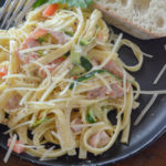 pile of fettucine alfredo with ham on black plate with slice of bread
