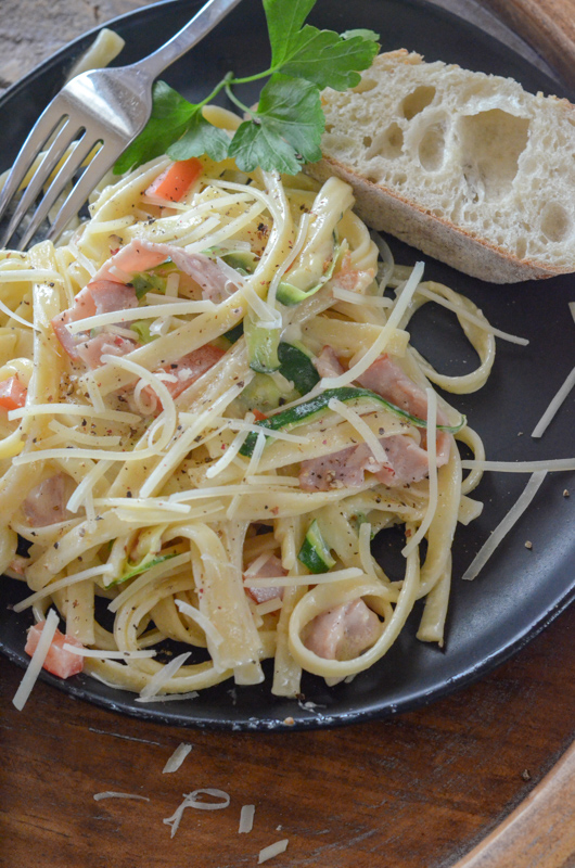 fettuccine alfredo with ham and zucchini on black plate with fork and bread 