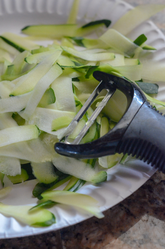 shaved zucchini ribbons on paper plate with vegetable peeler 
