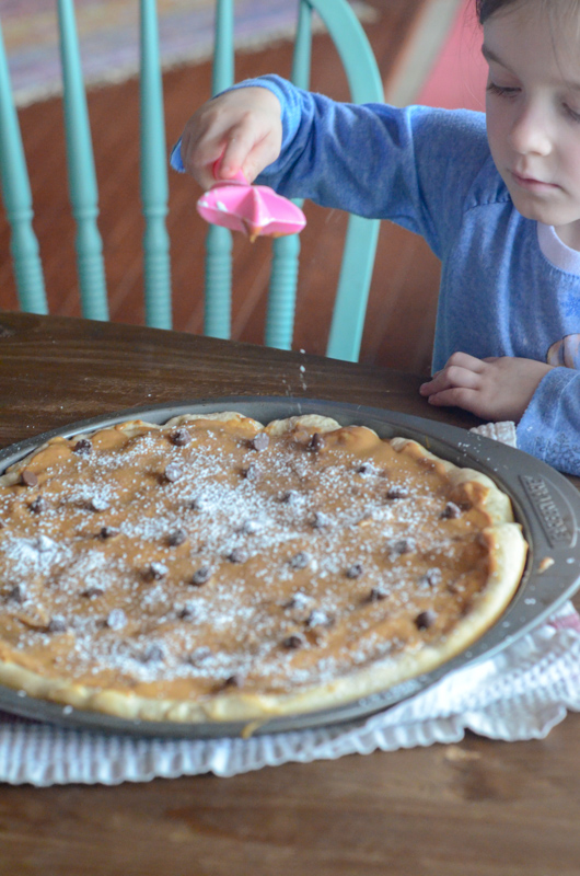 little girl sprinkles powdered sugar on dessert pizza 