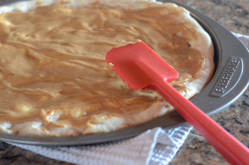 a peanut butter pizza on counter with only the layer of peanut butter on the crust and a red spatula