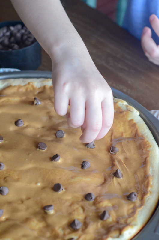 child drops chocolate chips onto a dessert pizza 