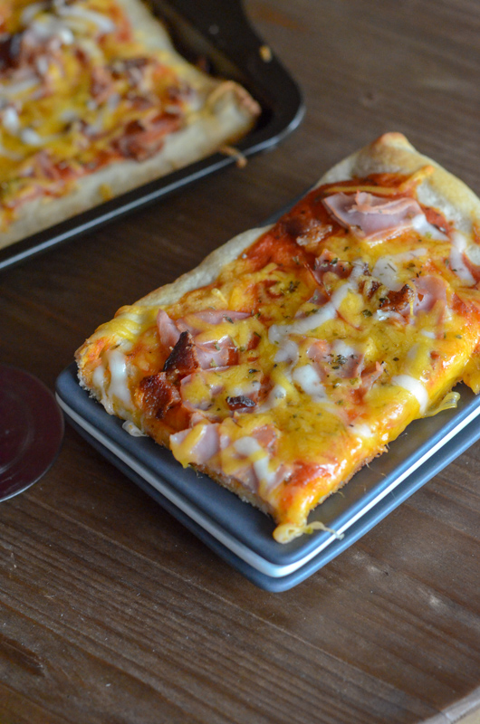 rectangular slice of bacon cheddar pizza with ham on stack of rectangular plates