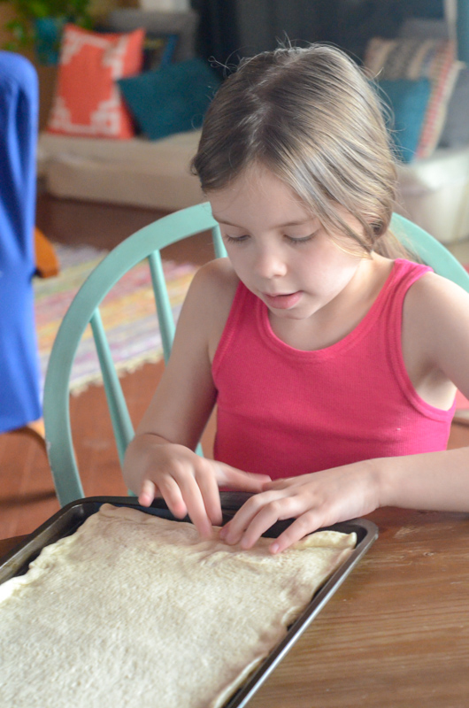 little girl stretches pizza dough on pan 