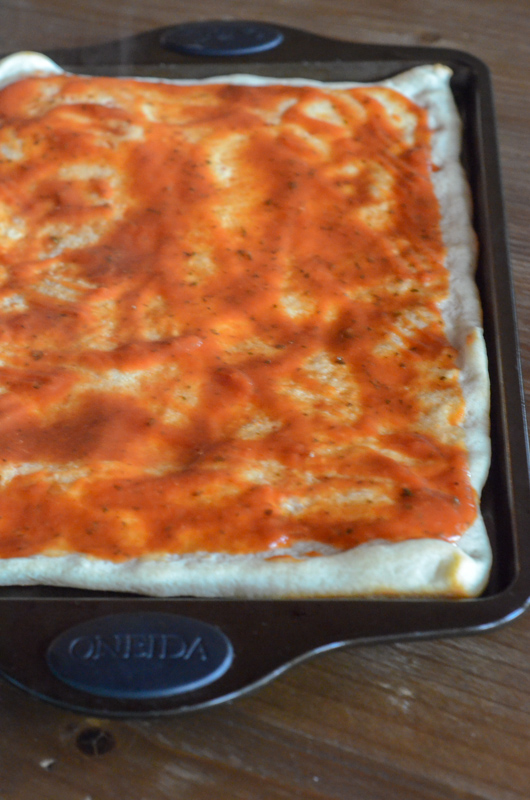 pizza sauce on rectangular pizza crust in pan for ham and cheese pizza