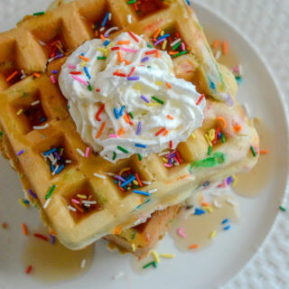 birthday cake waffles on white plate with syrup and sprinkles