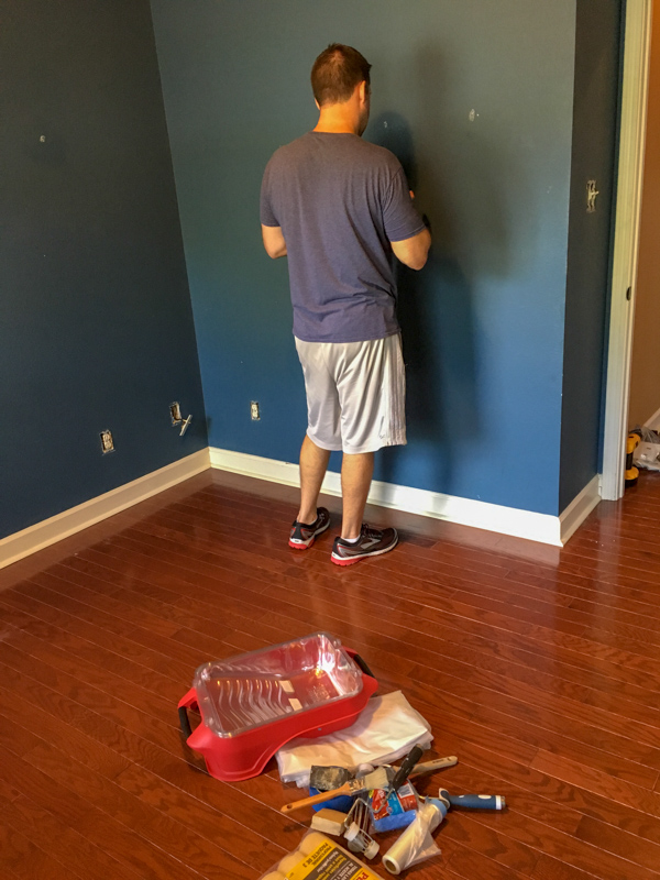 man preps a navy blue small bedroom for painting
