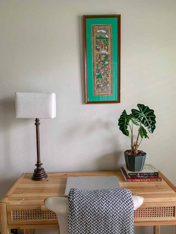 a light colored cane desk with a lamp, blue sun catcher wall hanging and Moroccan plant pot in an office guest room combo