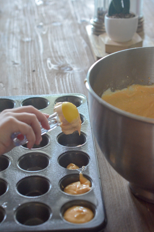 child's hand pours batter into mini muffin pan