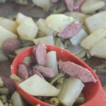 smoked sausage potato green beans sheet pan meal on black plate with sheet pan in back