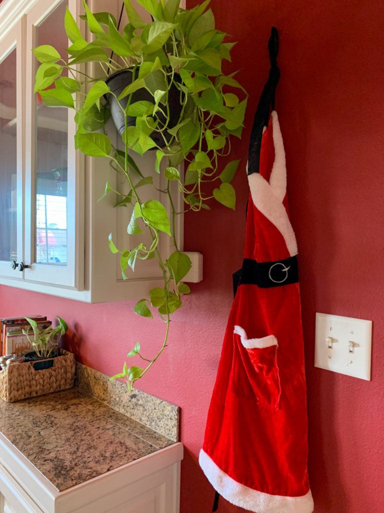 Christmas pothos hanging on hutch beside Mrs. Claus apron hanging on wall hook