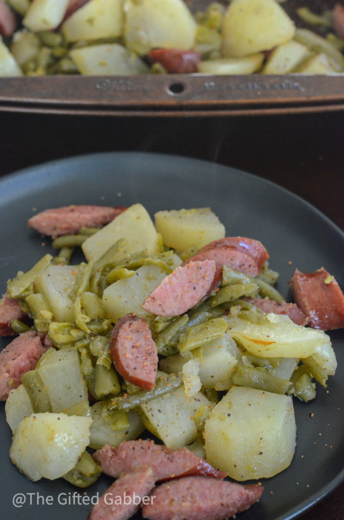 a black plate with sheet pan sausage potatoes and green beans meal