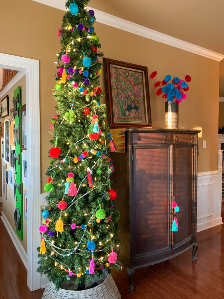 a boho Christmas tree and other boho Christmas decor in a room with a brown armoire and bright art