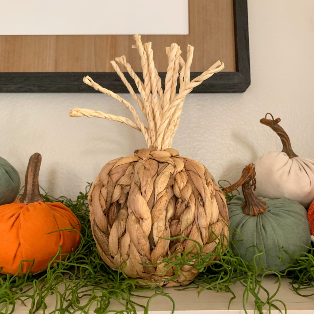 a basket woven pumpkin on a fall mantle with sevearl velvet and fabric pumpkins on either side 