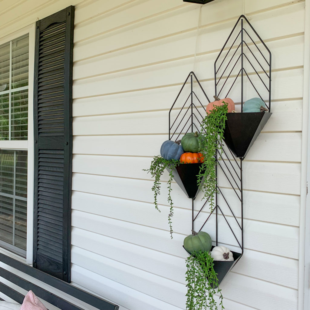 a black metal planter hangs on front porch with pumpkins and strings of pearls