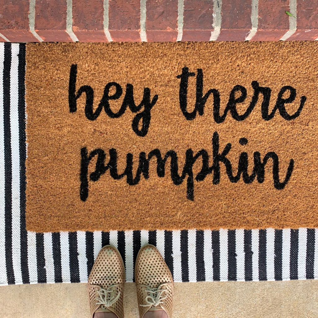 woman stands with gold shoes on top of "Hey There, Pumpkin" door mat on her fall porch