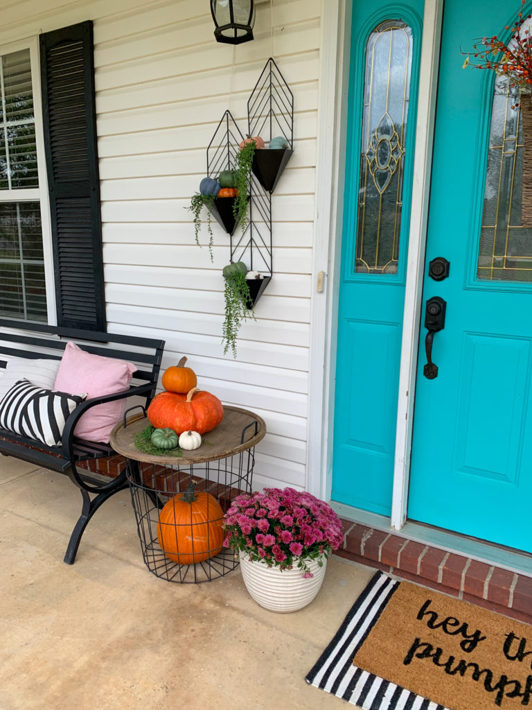 autumn decorations on a front porch with a hanging black planter with pumpkins inside