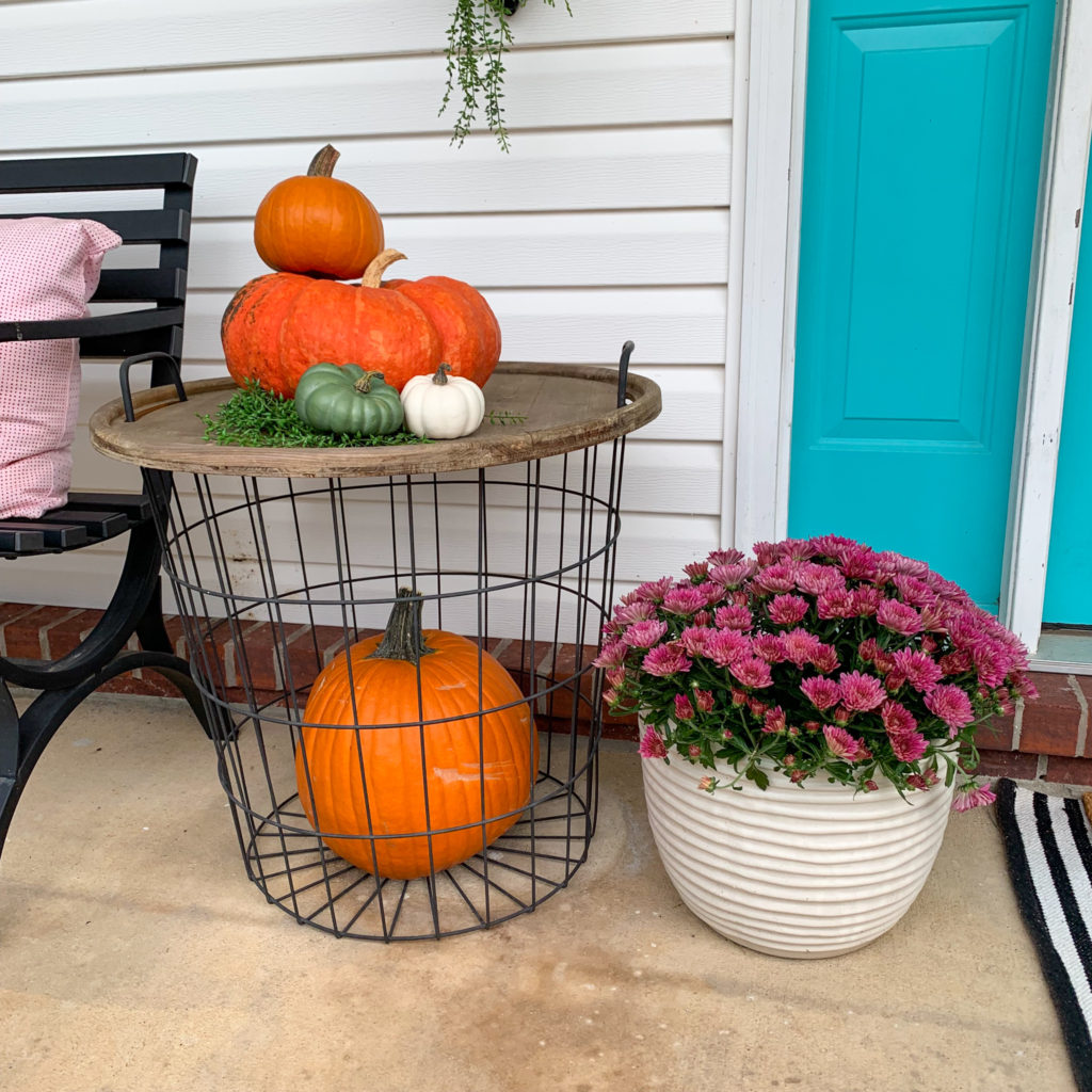 a pumpkin inside a metal basket table with more pumpkins on top and a purple mum for outdoor harvest decor