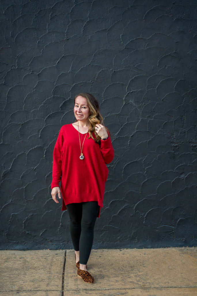 woman poses in red oversized sweater, black leggings and flat leopard print shoes in front of black wall in Benton, Arkansas